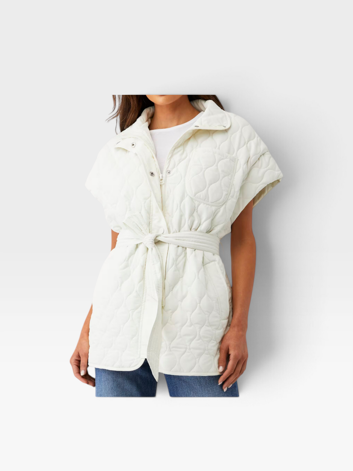Model wearing a cream BEACHRIOT quilted puffer vest with a belted waist and collar, styled with blue jeans.