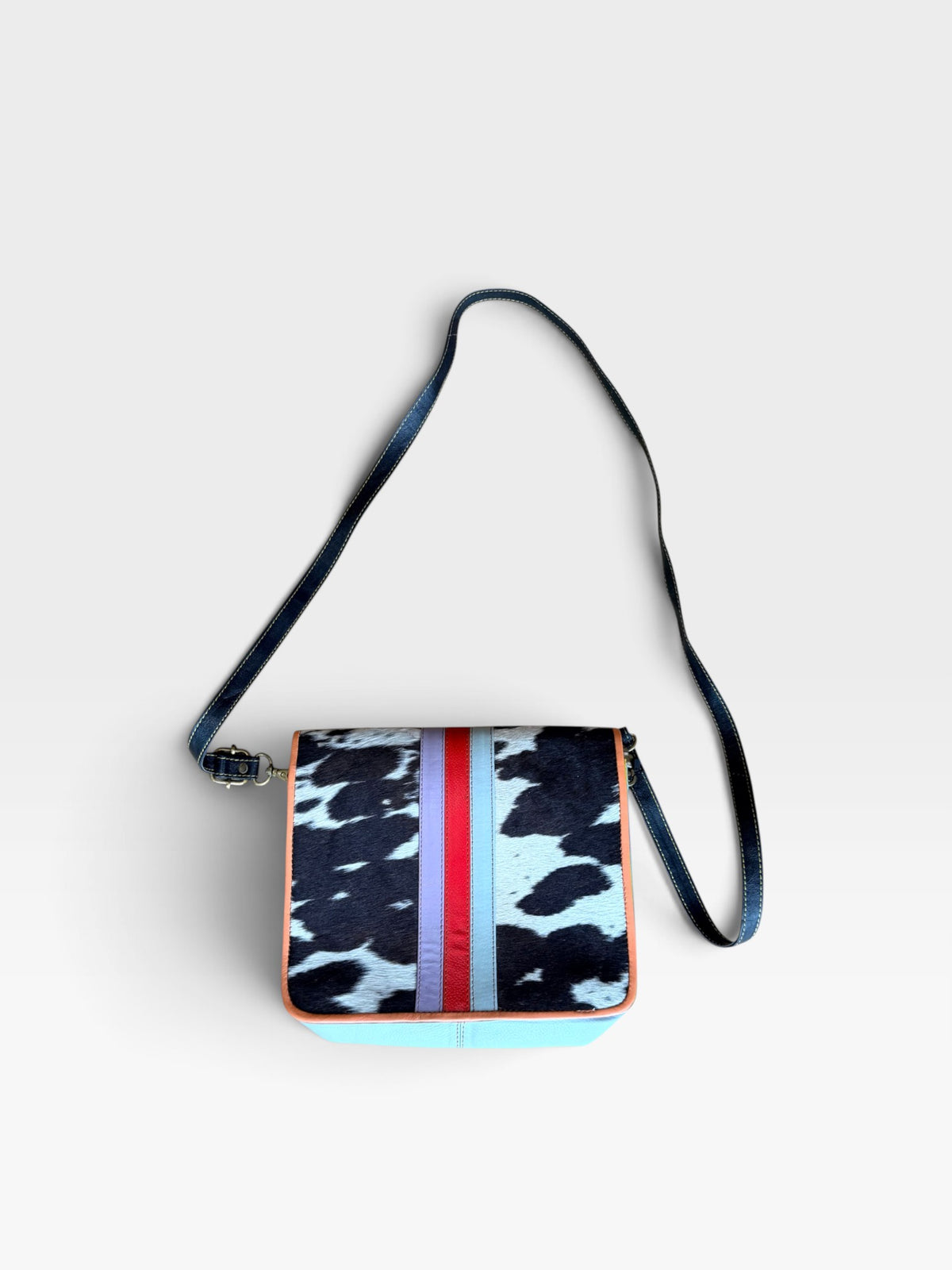 TheConsignmentBar Folklore Couture upcycled leather purse featuring a cow print pattern with red and purple stripes.
