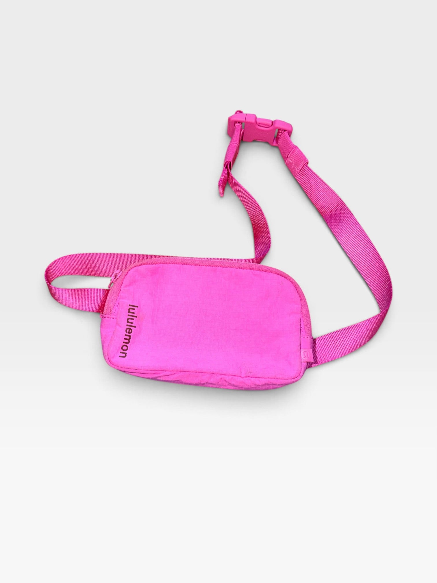 TheConsignmentBar Lululemon hot pink belt bag with adjustable strap and zipper closure resting on blue fabric
