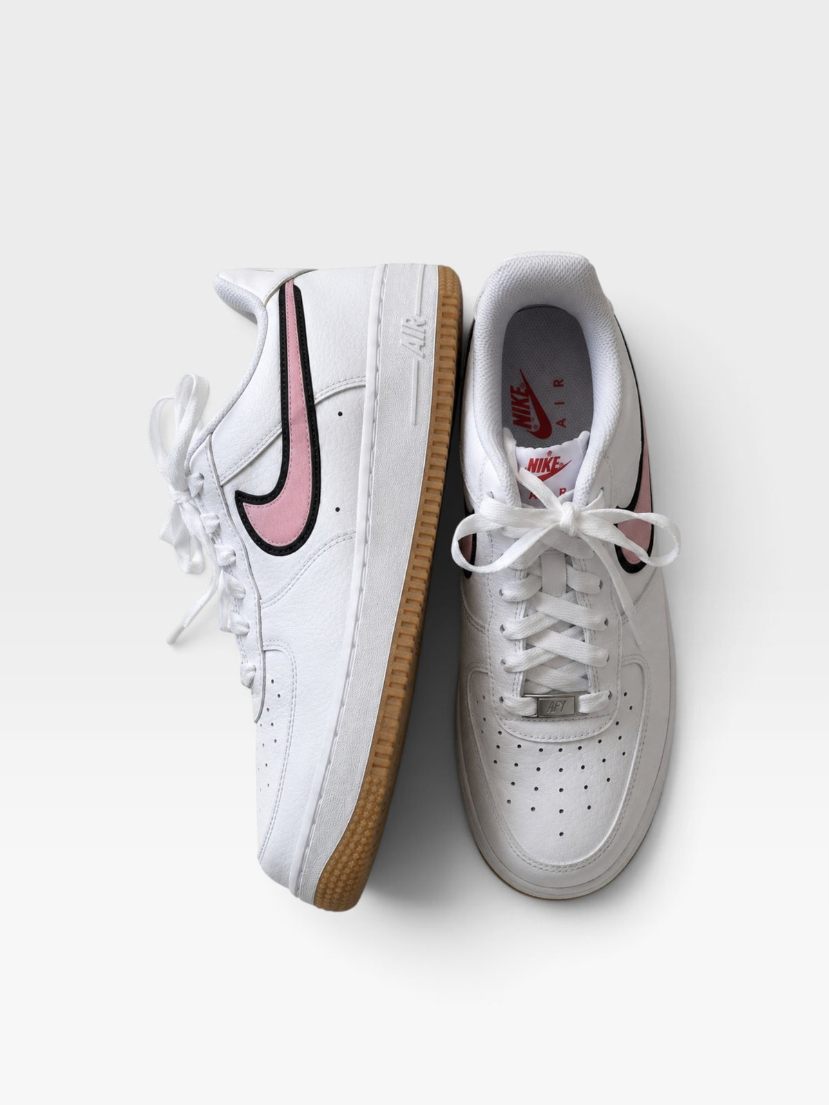 TheConsignmentBar Nike Air Force 1 sneakers in white leather with pink swoosh accents and gum rubber soles.