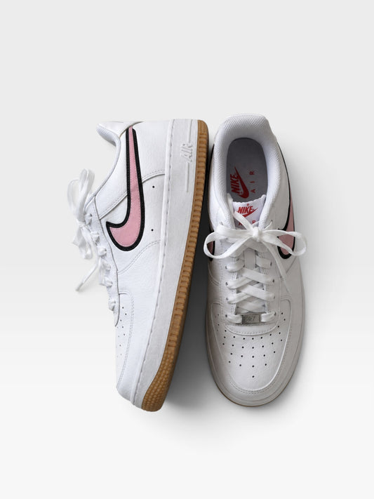 TheConsignmentBar Nike Air Force 1 sneakers in white leather with pink swoosh accents and gum rubber soles.