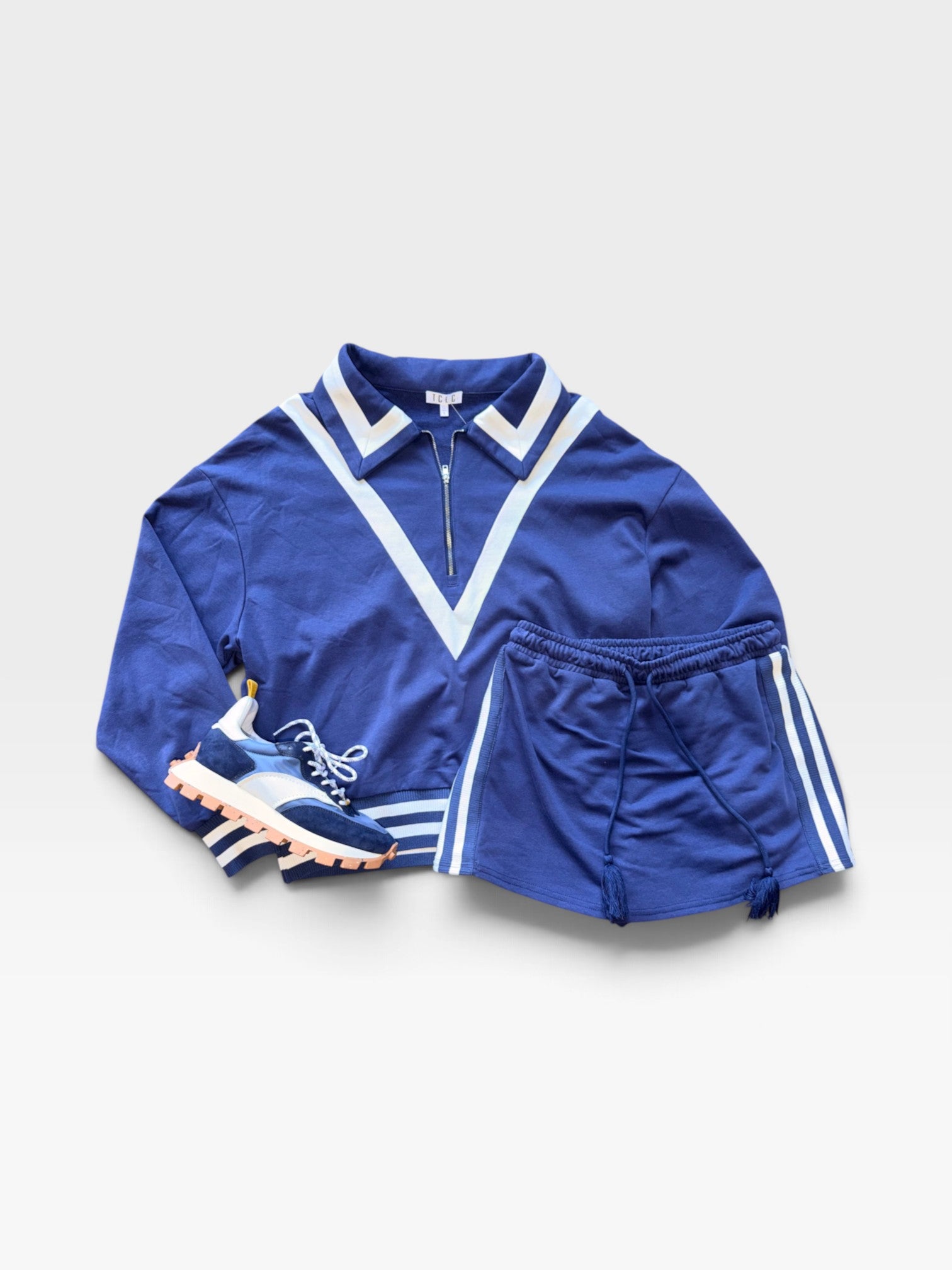 TheConsignmentBar TCEC blue and white collared zip-up sweatshirt and matching skort set with athletic sneakers.